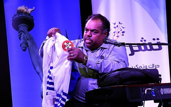 Black musician Daryl Davis holds up the robes of a Ku Klux Klan member on stage