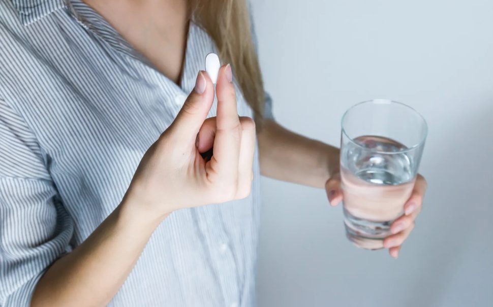 a woman holds a pill and a glass of water