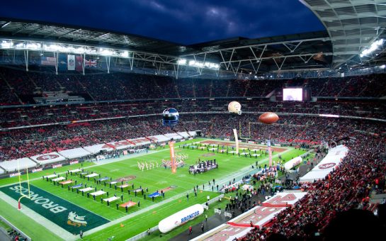 Wembley Stadium pitch covered with flags and people in pre match build up to NFL match