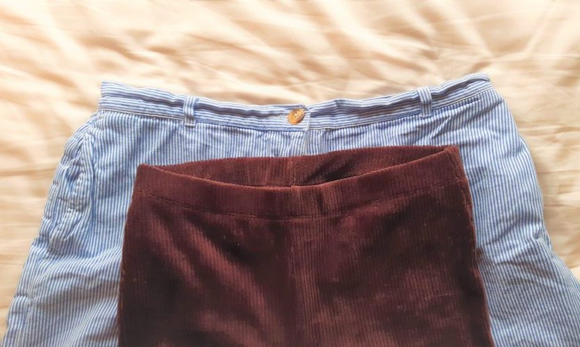 A pair of trousers with a small waistband lying on top of a pair of shorts with a larger waistband