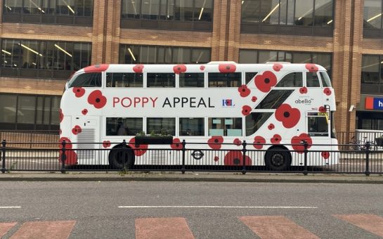 A bus with poppy appeal on the side driving down a street