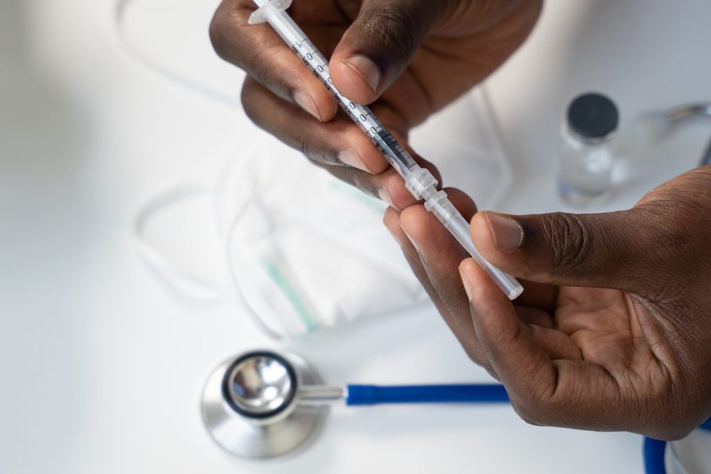 Stock image of a person holding a medical needle with a stethoscope in the background 