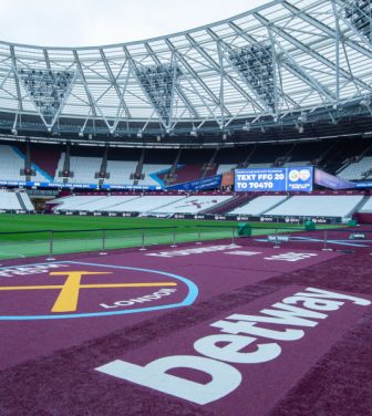 Pitch side image of the the London Stadium interior with the West Ham United badge in view.