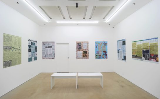 A white walled gallery showing Webb-Ingall's posters, with two white benches in the middle of the room.