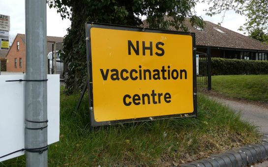 A yellow sign with the words "NHS vaccination centre" displayed outside a building