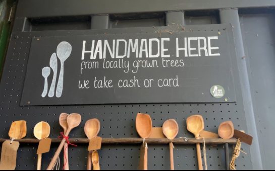 A sign detailing the handmade spoons made at London Greenwood. The spoons sit hanging from a shelf below.