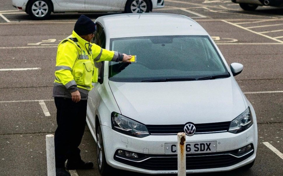 Someone putting a parking ticket on a car