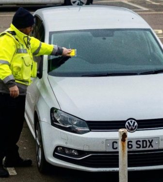 Someone putting a parking ticket on a car