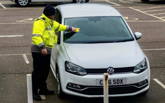 Someone putting a parking ticket on a car