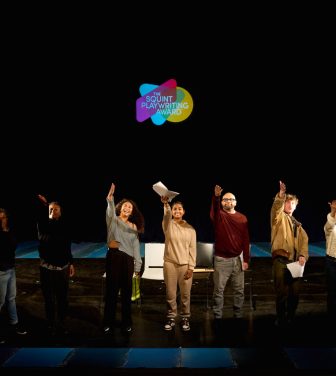 A photo of the Arts Council England funded Squint Playwriting Award, with nine young writers on a stage gesturing towards the sky