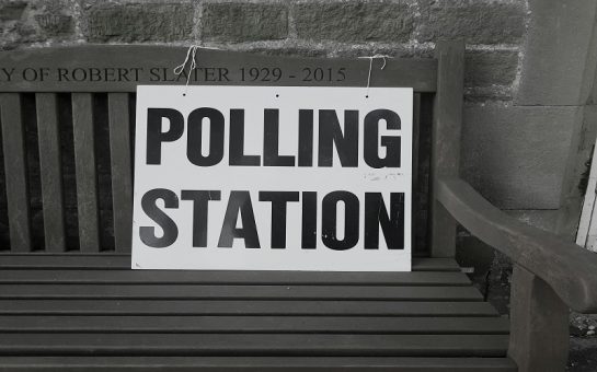 A picture of a sign saying "Polling Station" tied to a wooden bench. Photo by Steve Houghton-Burnett on Unsplash