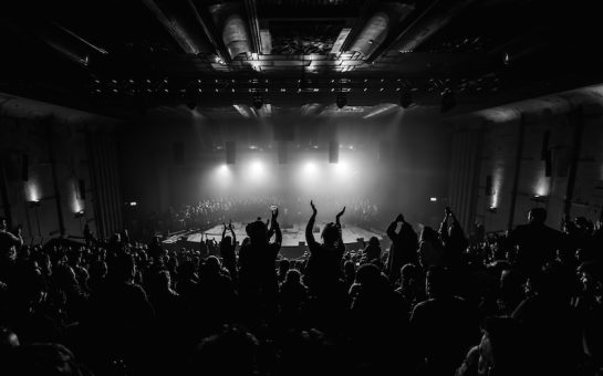 Choir performing at sell-out Hackney show, with standing-ovation from audience in the foreground.