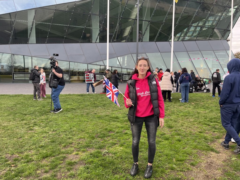 Lady in pink hoodie waves Union Jack flag outside City Hall, London.