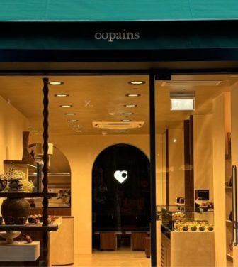 Copains London bakery storefront green canopy with business name and warm bakery interior