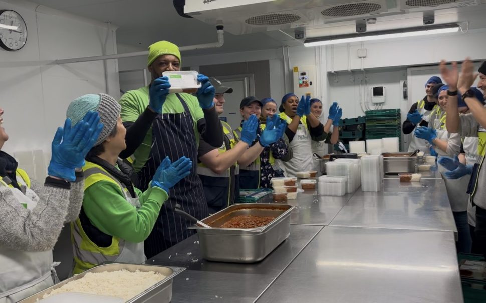 Chef holding up packaged meal surrounded by kitchen staff