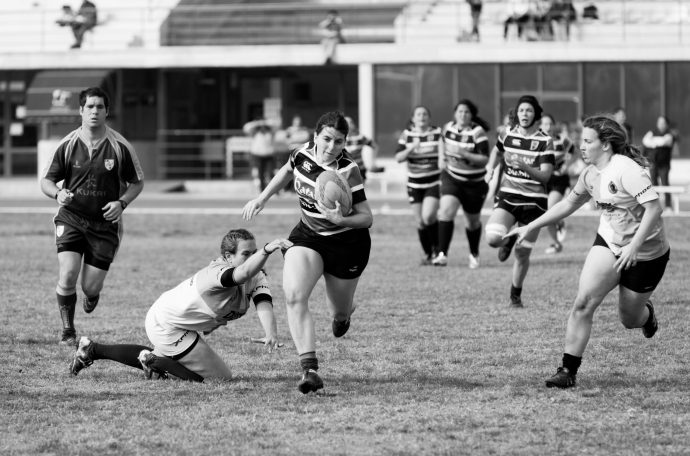 The photograph is of female rugby players. One lady attempting to tackle another while she is running with the ball.