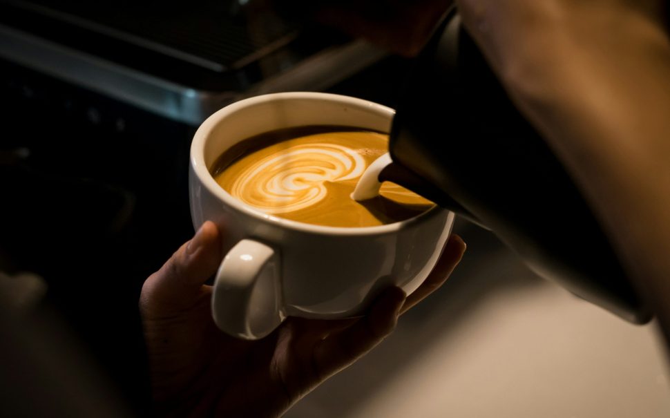 A coffee cup being held with latte art being poured