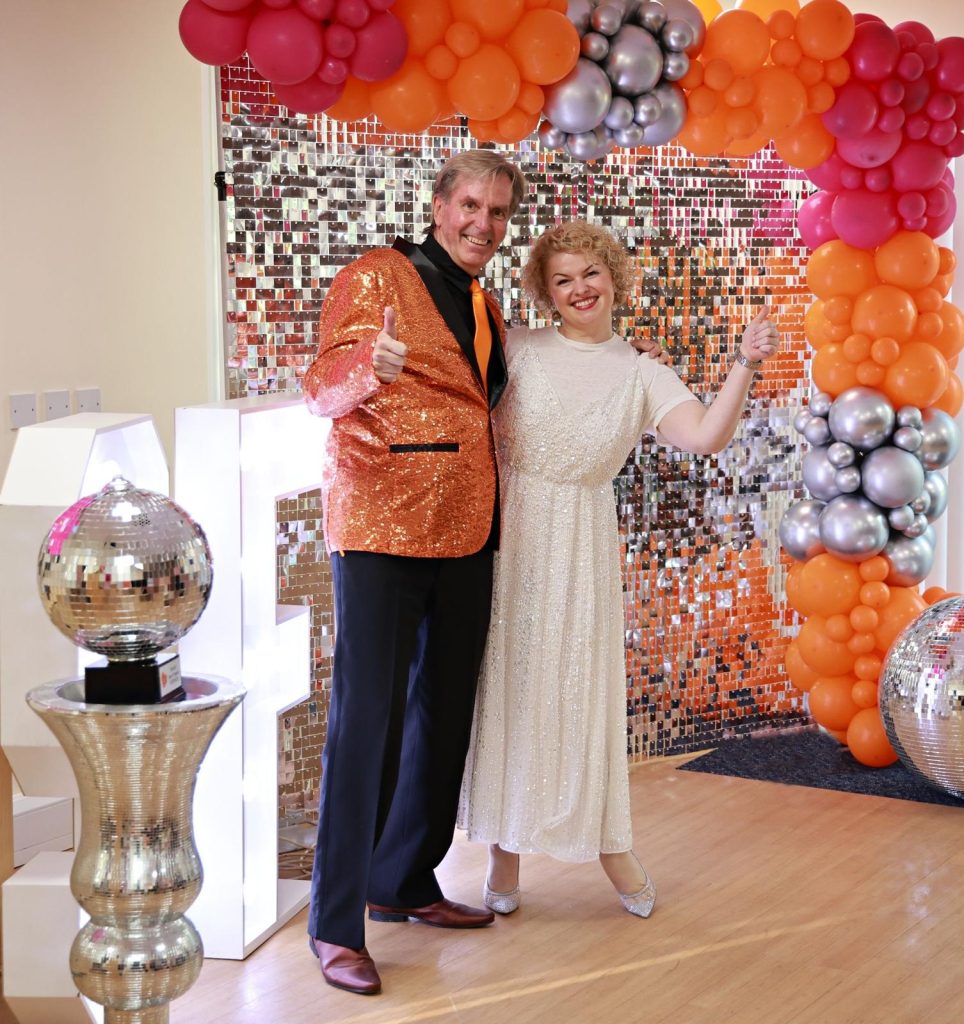 Hospice ambassador Skip Atkins and his professional partner Jolita Kudoke are dressed up and posing in front of the glitterball trophy after being paired up at the Strictly St Francis launch night in June.
