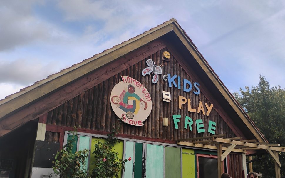 Playhouse at Homerton Grove Adventure Playground with sign 'Kids Play Free'